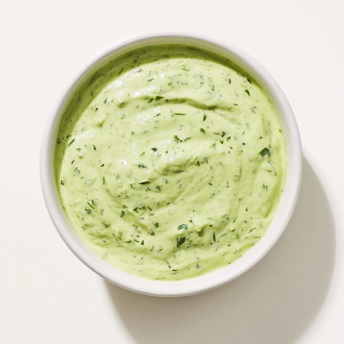 Bright green Green Goddess Dressing in a jar, garnished with fresh tarragon and parsley leaves, perfect for dipping crunchy veggies.  