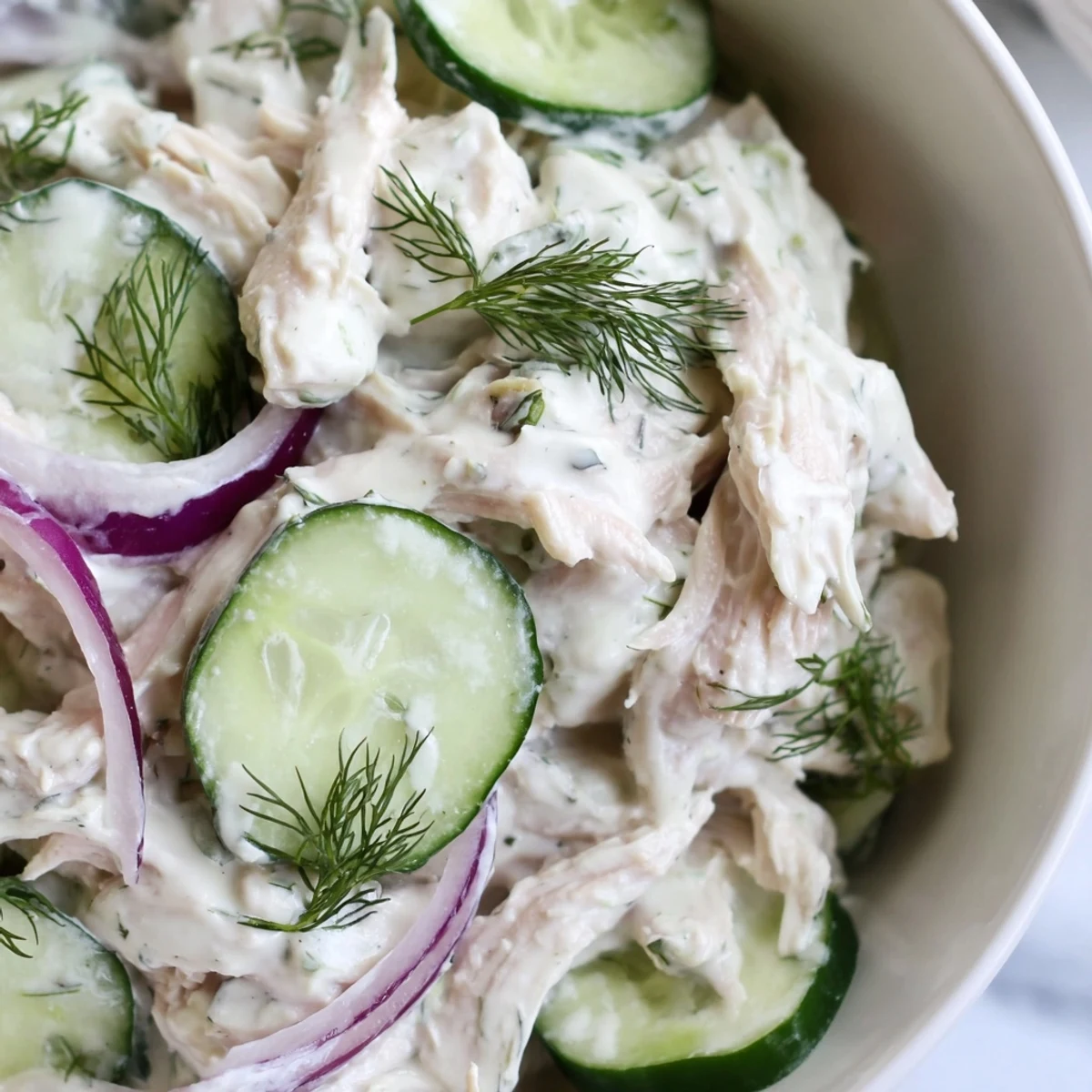 A close-up of creamy cucumber chicken salad served in a white bowl, featuring tender shredded chicken, crisp cucumber slices, and fresh dill.