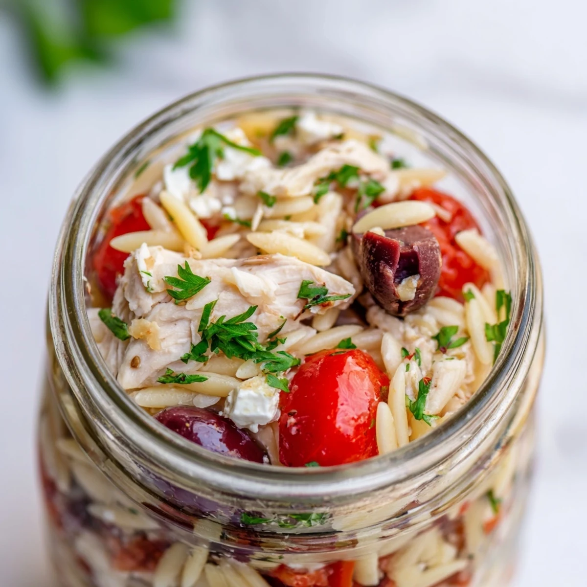 Mediterranean-style meal prep jars filled with orzo pasta, juicy chicken, crunchy veggies, and creamy feta, ready to serve.