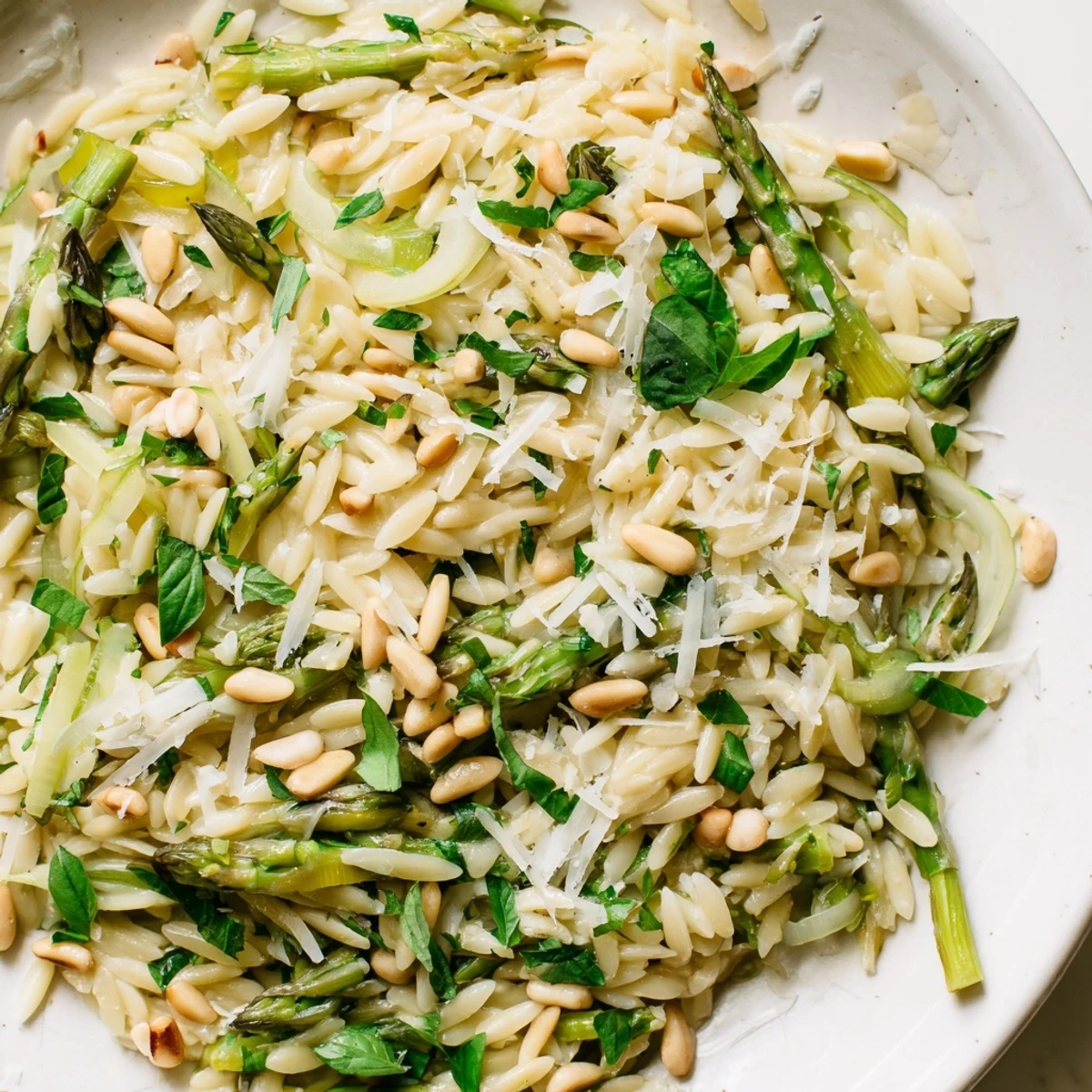 A fresh spring bowl of Asparagus Lemon Orzo Salad topped with herbs and shaved Parmesan, ready to serve.
