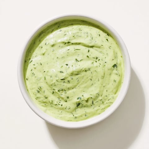 Bright green Green Goddess Dressing in a jar, garnished with fresh tarragon and parsley leaves, perfect for dipping crunchy veggies.  