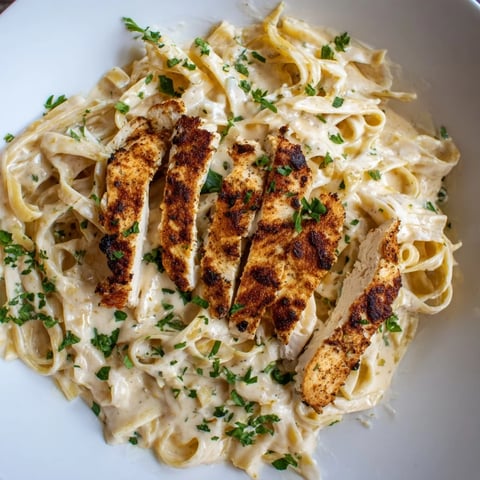 Golden-brown Cajun chicken slices rest atop creamy fettuccine Alfredo in a rustic white bowl, garnished with fresh parsley and extra Parmesan.