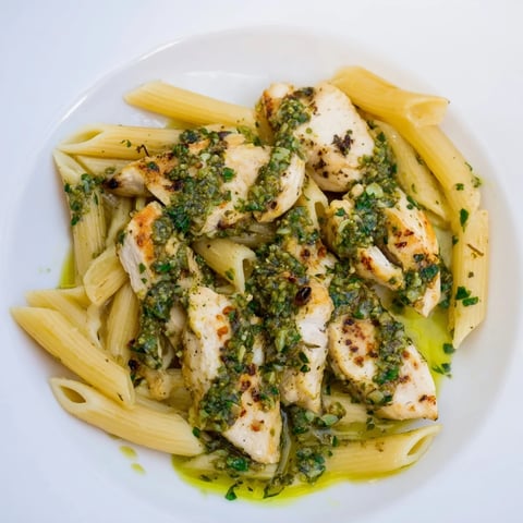 The image shows grilled Chimichurri Chicken Pasta with green parsley sauce coating penne and sliced chicken.  