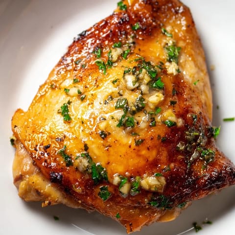 A top-down view of four crispy-skinned Garlic Butter Chicken Thighs on a platter, garnished with parsley and lemon wedges.