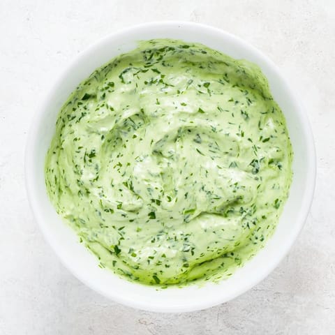 A creamy bowl of Green Goddess Dressing drizzled over a colorful salad with avocado and grilled chicken for a healthy lunch.  
