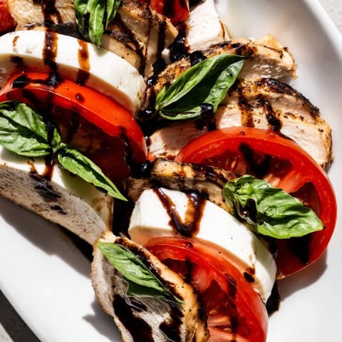 Sliced grilled chicken breast layered with ripe tomato rounds and creamy mozzarella, garnished with basil leaves and a balsamic dressing.