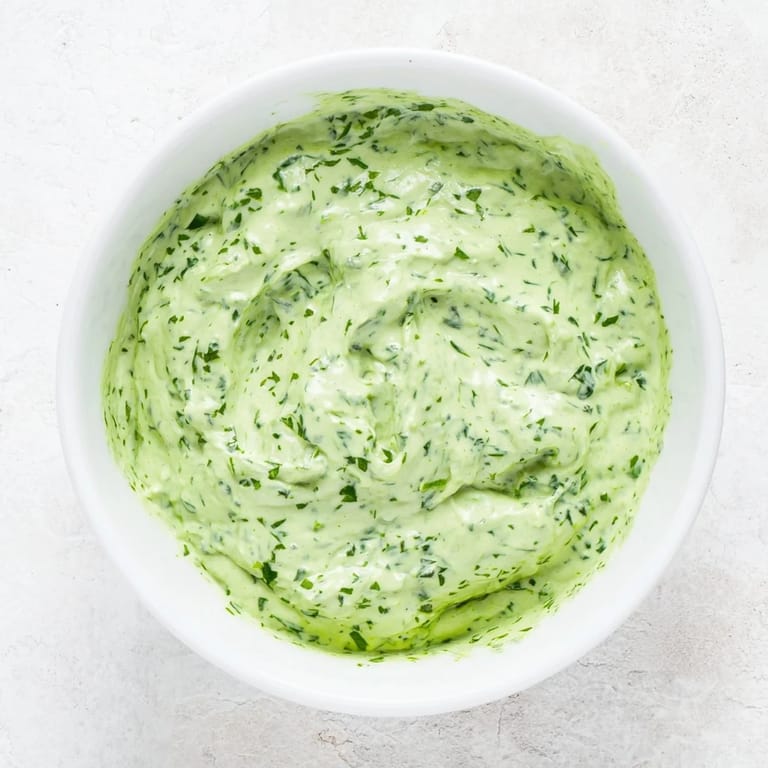 A creamy bowl of Green Goddess Dressing drizzled over a colorful salad with avocado and grilled chicken for a healthy lunch.  