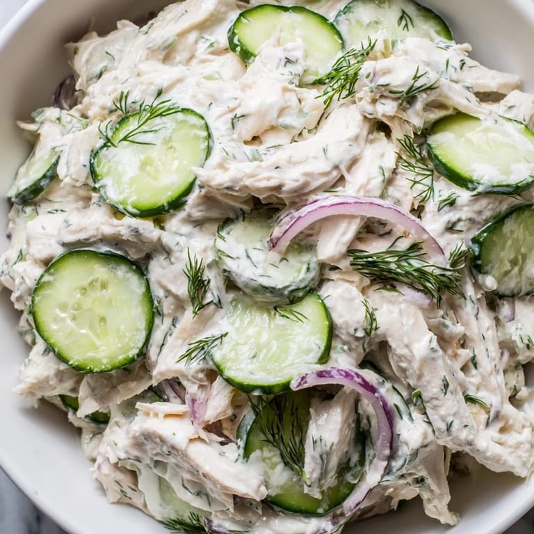 Bowl of creamy cucumber chicken salad garnished with green onions and a lemon wedge, ideal for a refreshing light lunch or summer meal.