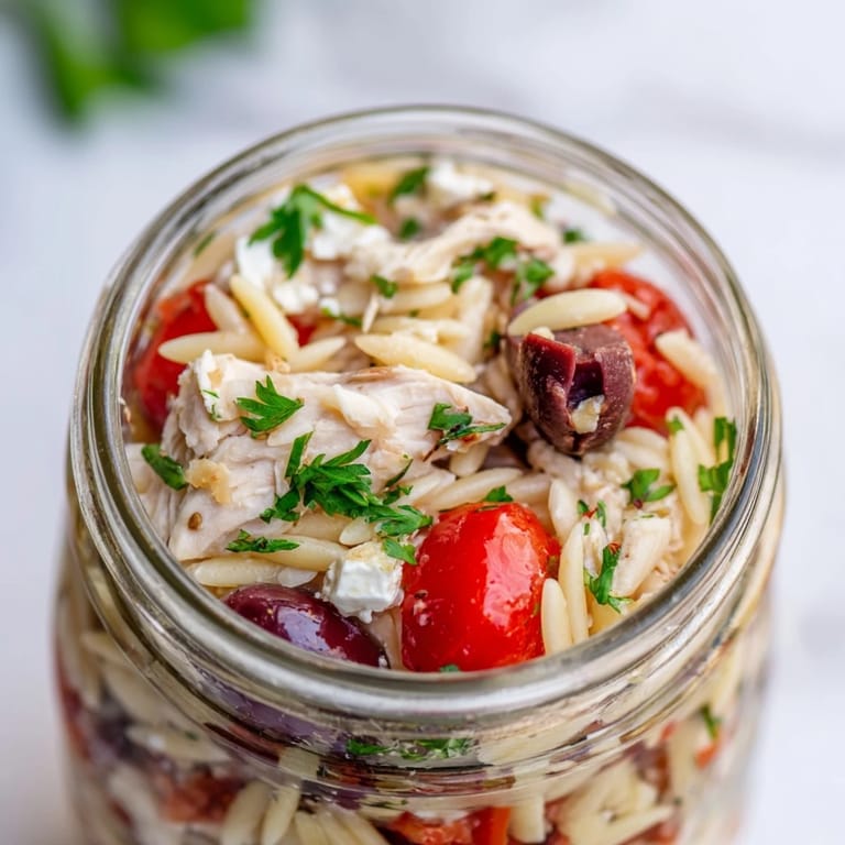 Mediterranean-style meal prep jars filled with orzo pasta, juicy chicken, crunchy veggies, and creamy feta, ready to serve.
