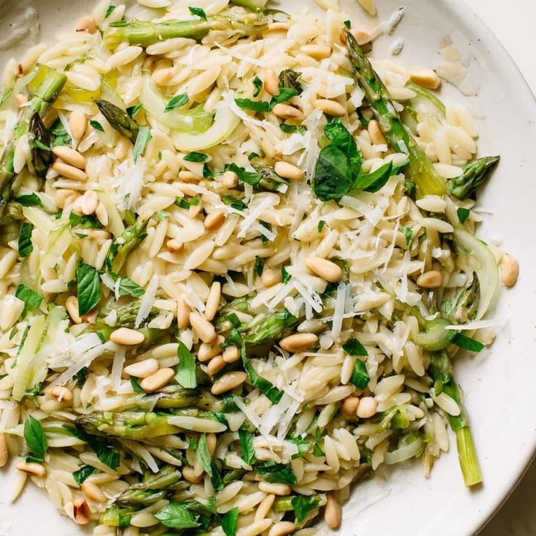 A fresh spring bowl of Asparagus Lemon Orzo Salad topped with herbs and shaved Parmesan, ready to serve.