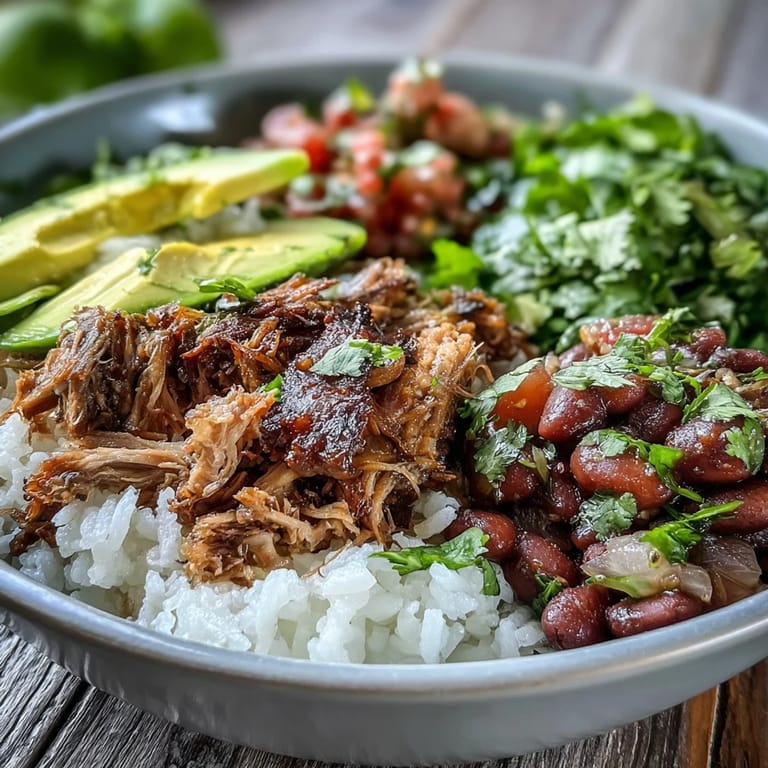 A close-up of a hearty carnitas bowl with seasoned pinto beans, cilantro, and zesty lime wedges for a Mexican-inspired meal.